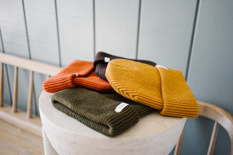 Scout Beanies in Rust, Brown, Gold and Green stacked on a stone pedestal