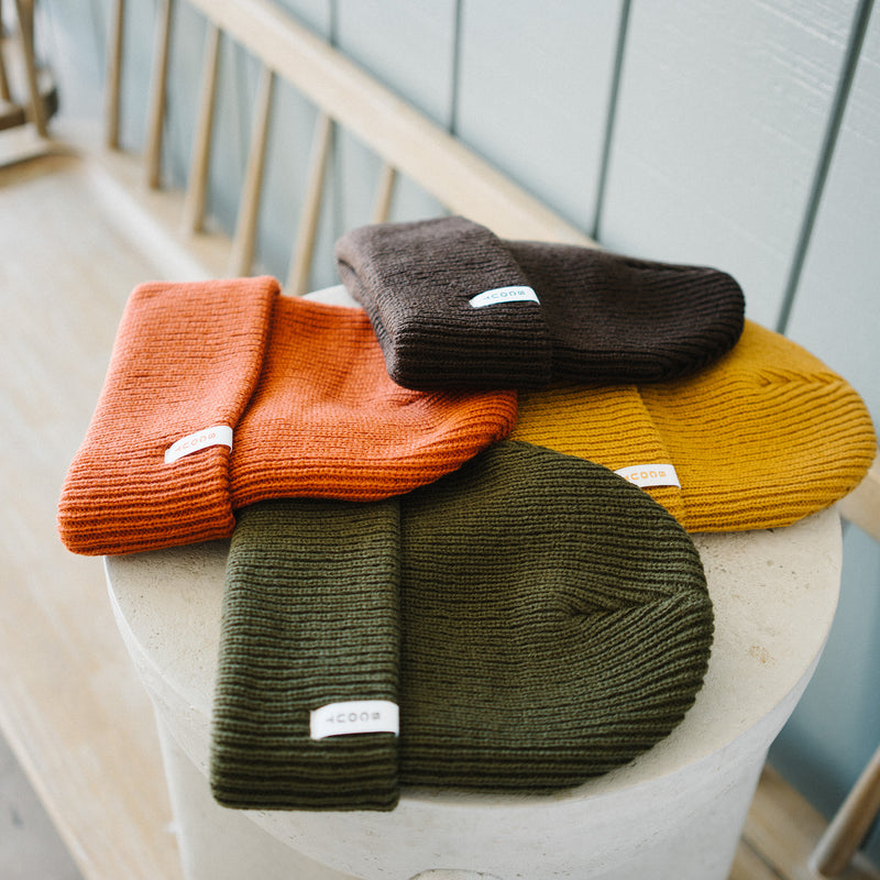 Scout Beanies in Rust, Brown, Gold and Green, stacked on a stone pedestal