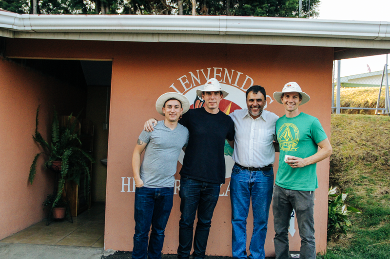 4 people in sun hats pose in front of a Bienvenidos mural on a building in Costa Rica