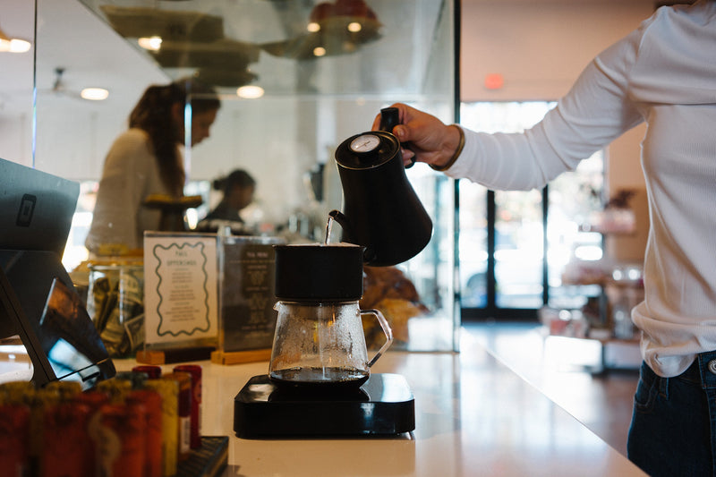 A barista pouring water from a gooseneck kettle into a pour over at the Scout Morro Bay bar