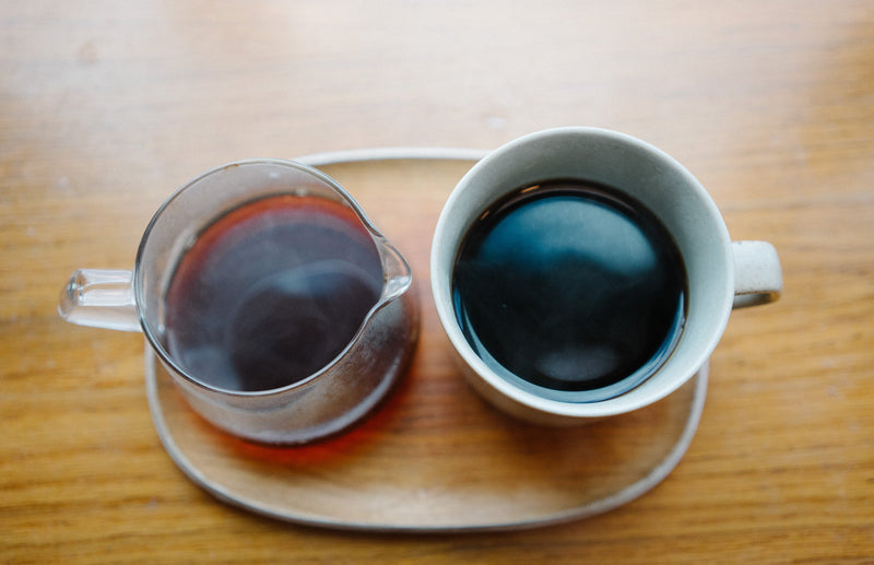 A pour over server and a cup of black coffee on a wooden tray, seen from above