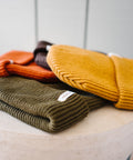 Scout Beanies in Rust, Brown, Gold and Green, laid on a stone pedestal