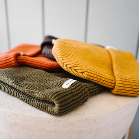 Scout Beanies in Rust, Brown, Gold and Green, laid on a stone pedestal