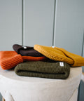 Scout Beanies in Rust, Brown, Gold and Green, laid on a stone pedestal by a wooden bench