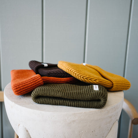 Scout Beanies in Rust, Brown, Gold and Green, laid on a stone pedestal by a wooden bench